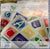 A packaged children's alphabet card set by Polly's Place, featuring colorful square cards with white uppercase letters on a multicolored illustrated background. The front shows the brand name 'Polly's Place' and a white sticker label with SKU information.